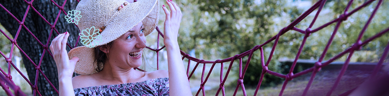 A smiling woman relaxing in a hammock outside. 