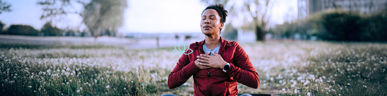 Person wearing a red jacket stands in a field of flowers with hands placed on chest.