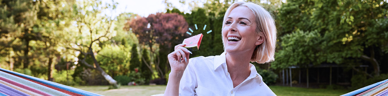 Person outdoors holding a small paper house while sitting on a hammock in a yard.
